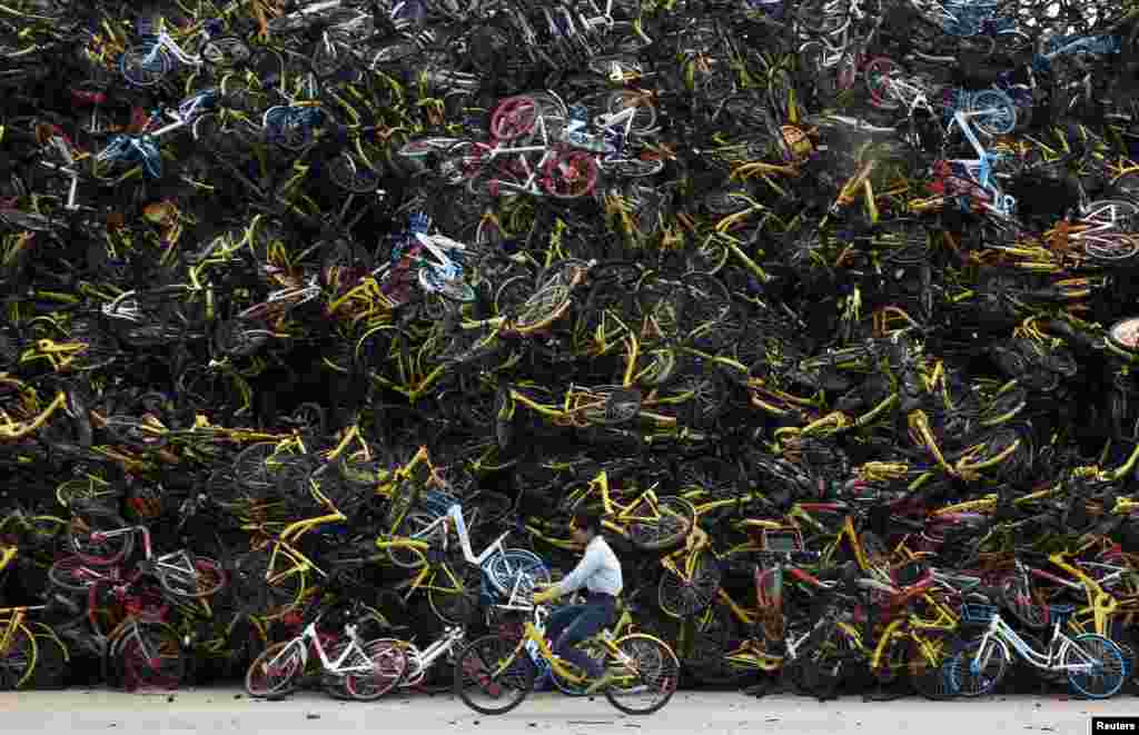 A worker rides a shared bicycle past piled-up shared bikes at a vacant lot in Xiamen, Fujian province, China.