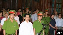 Tiến sĩ Cù Huy Hà Vũ đứng giữa 2 công an tại phiên tòa xử ông ở Hà Nội hôm 2 tháng 8, 2011