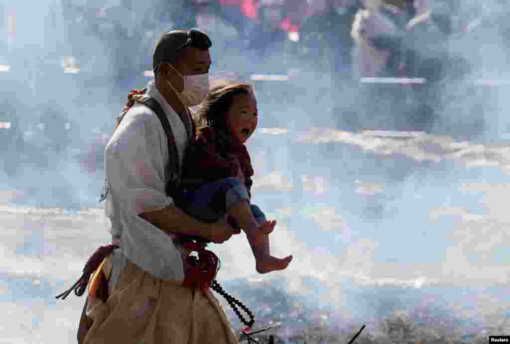 A Buddhist monk wearing a protective mask, amid the coronavirus disease (COVID-19) outbreak, carries a child as he walks across smoldering hot ground at the fire-walking festival, called hiwatari matsuri in Japanese, at Mt.Takao in Tokyo, Japan.