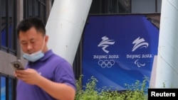 资料照：2021年7月30日，在北京奥组委总部，一名男子在走过北京2022年冬奥会和冬残奥会的标志时使用手机。