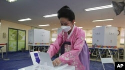 一位戴上口罩避免新冠病毒传播的女士在韩国首尔的投票所投下国会选举票(2020年4月15日)