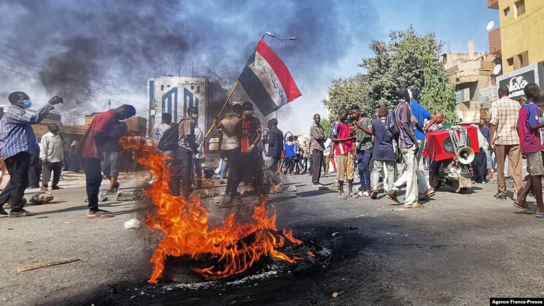 Sudanese protesters walk past burning tires as they rally to protest against the Oct. 2021 military coup, in the capital Khartoum, on Jan. 9, 2022.