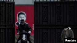 戴着口罩的行人从上海街头一个有着习近平画像的大门前经过。（2020年2月10日）