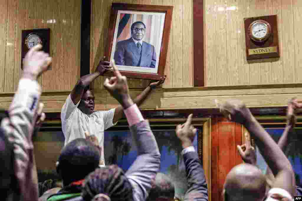 A man removes a portrait of former Zimbabwean President Robert Mugabe from the wall at the International Conference Center, after his resignation in Harare. Mugabe stepped down after a 37-year reign of brutality and autocratic control crumbled within days of a military takeover.