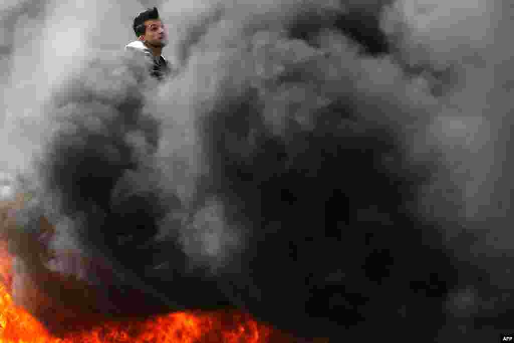 A Palestinian protester is seen amidst the smoke from burning tires during clashes with Israeli forces following a demonstration near the Israeli settlement of Beit El in the Israeli occupied West Bank.